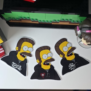 May include: Three die-cut stickers featuring a cartoon character with yellow skin, brown hair, a mustache, and glasses. The character wears a black hoodie with white text. One sticker has a heart with a skull.