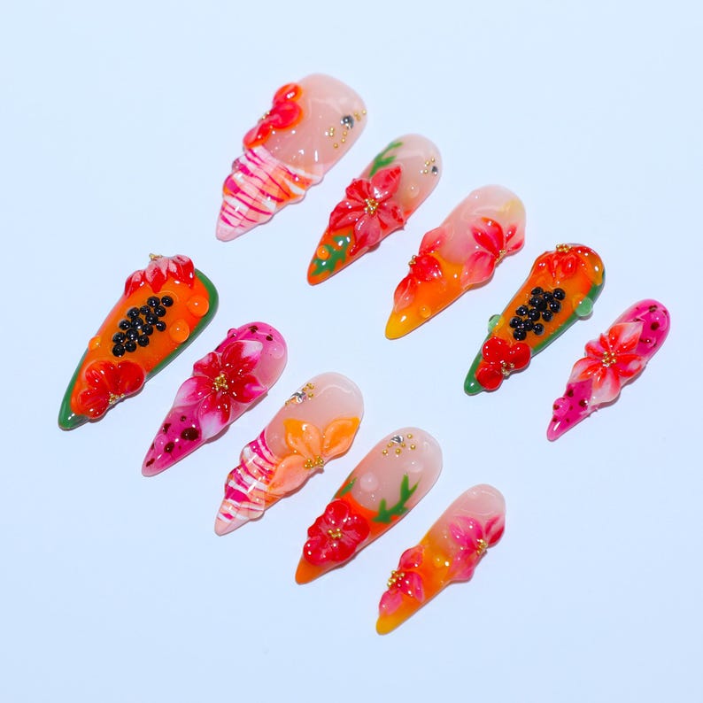 May include: A set of ten press-on nails featuring vibrant 3D designs. The nails display various motifs including bright orange papaya slices with black seeds, red and pink floral patterns, and striped accents, all embellished with small gold beads.