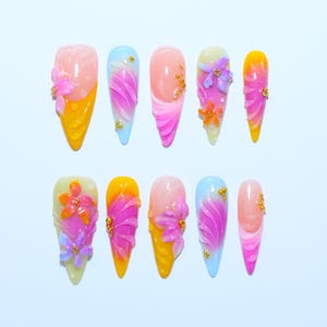 May include: A set of ten press-on nails featuring almond and stiletto shapes with a vibrant color palette of yellow, pink, blue, and orange. The designs include 3D floral accents, layered petal patterns, and small gold metallic bead embellishments.