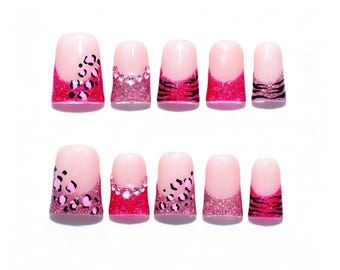 May include: A set of ten press-on nails featuring a nude base with vibrant pink tips. The designs include black leopard spots, pink glitter, clear rhinestones, and black tiger stripes across the various nail sizes and shapes in the collection.