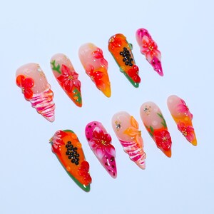 May include: A set of ten press-on nails featuring a variety of vibrant designs including 3D floral patterns, papaya fruit motifs with black seeds, pink and white striped accents, and small gold bead embellishments on a translucent base.
