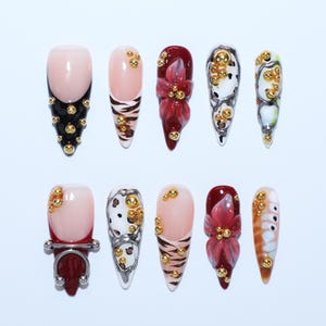 Peut inclure: Un ensemble de dix faux ongles présentant divers motifs, dont des pointes françaises noires avec des clous dorés, des rayures de tigre, des motifs floraux rouge foncé, des textures tachetées noir et blanc et un ongle orné d'un anneau en métal argenté.