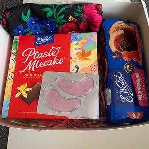 May include: A gift box with a selection of treats. It includes a box of E. Wedel Ptasie Mleczko vanilla marshmallows in chocolate, eye patches, raspberry jaffa cakes, and a floral scarf with a black background.