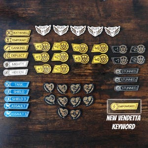 May include: A collection of wooden game tokens featuring various shapes and text including BUFF +1, DEATHKNELL, TEMPORARY, GANKING, DEFLECT, MIGHTY, HIDDEN, TANK, SHIELD, ASSAULT, STUNNED, EMPOWERED, and heart-shaped tokens with negative numerical values.