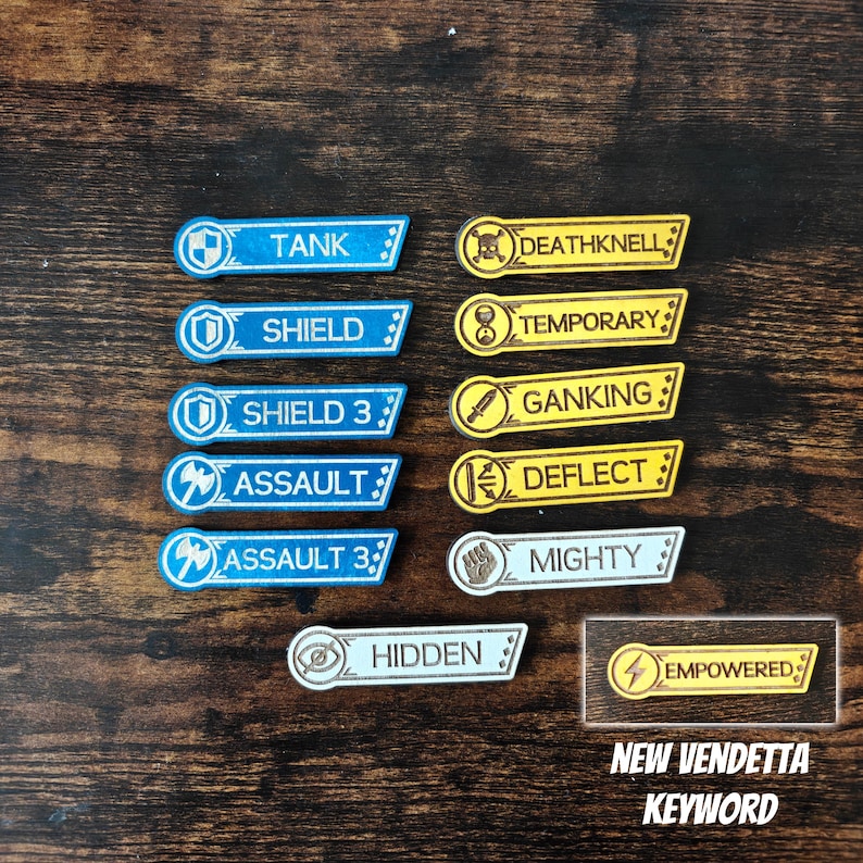 May include: A collection of rectangular game tokens featuring icons and text labels including Tank, Shield, Shield 3, Assault, Assault 3, Deathknell, Temporary, Ganking, Deflect, Mighty, Hidden, and Empowered, with the latter labelled New Vendetta Keyword.