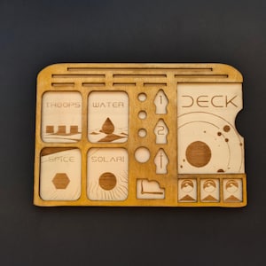 May include: A wooden game organiser with compartments for game pieces and a deck of cards. The compartments are labelled "Troops", "Water", "Spice", and "Solari". The deck of cards is labelled "Deck".
