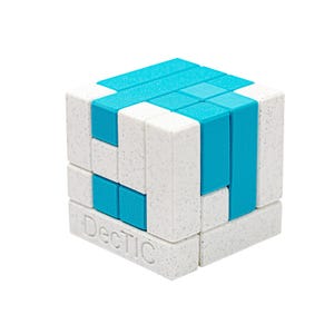 Op de afbeelding: Een witte en turquoise kubuspuzzel met het woord "DecTIC" op één kant gedrukt. De puzzel heeft een gespikkelde textuur op de witte stukken en effen turquoise stukken. De kubus is een hersenkraker.