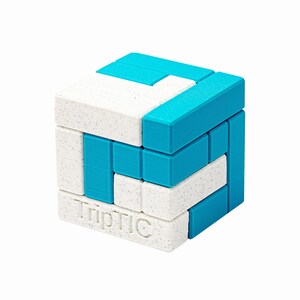 Könnte beinhalten: Ein Würfelpuzzle mit ineinandergreifenden weißen und blauen Teilen. Die weißen Teile haben eine gesprenkelte Textur, und die blauen Teile sind einfarbig. Das Wort "TripTIC" ist auf einer Seite geprägt. Ein Denkspiel.