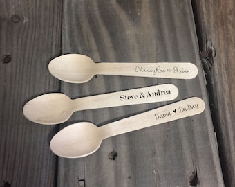May include: Three wooden spoons with personalised names and a heart symbol. The spoons are on a wooden surface.