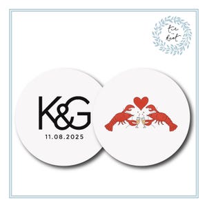 May include: Two white round coasters. One coaster features the letters "K&G" in black with the date "11.08.2025" below. The other coaster has two red lobsters toasting champagne glasses with a red heart above.