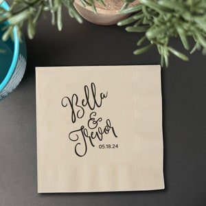 May include: A beige paper napkin with black calligraphy that reads "Bella & Trevor" and the date "05.18.24".