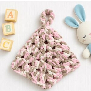 May include: A pink, brown, and white crocheted baby toy with a loop at the top. The toy is shaped like a triangle and has a soft, fuzzy texture.