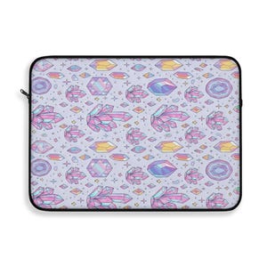 Puede incluir: Una funda para portátil con un patrón repetido de cristales, gemas y estrellas de colores sobre un fondo morado claro. Los cristales son en tonos rosa, azul, amarillo y morado.