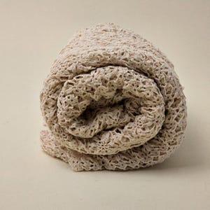 May include: A cream-coloured crocheted fabric rolled up into a ball. The fabric is made of a delicate, open-weave pattern.