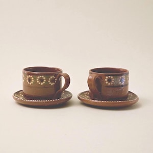 Peut inclure: Deux tasses à café en céramique marron avec soucoupes assorties. Chaque tasse et soucoupe présente un motif décoratif de points blancs et d'accents verts. Les tasses ont des anses incurvées.