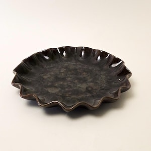 May include: A dark brown ceramic plate with a ruffled edge. The plate has a glossy finish and a textured surface. The plate is round and appears to be handmade. This decorative plate is suitable for serving food.