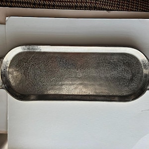 Puede incluir: Una bandeja ovalada plateada con dos asas redondeadas. La bandeja tiene una superficie texturizada y est&aacute; sobre un fondo blanco. La bandeja mide aproximadamente 30 cm de largo.