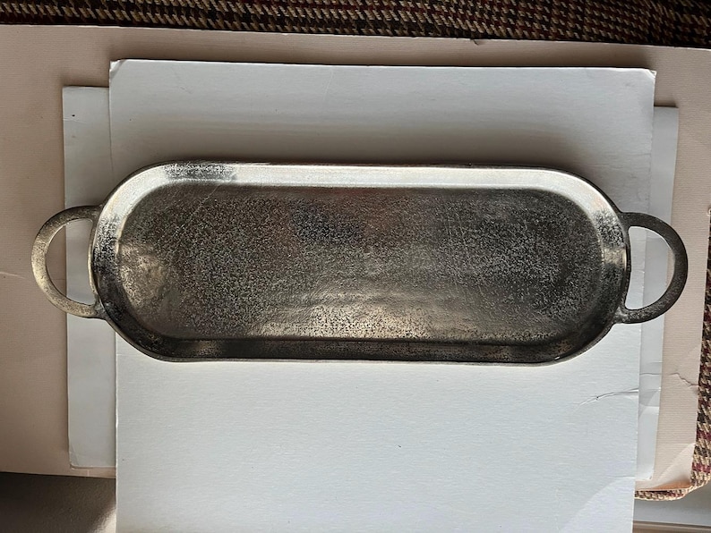 Puede incluir: Una bandeja ovalada plateada con dos asas redondeadas. La bandeja tiene una superficie texturizada y est&aacute; sobre un fondo blanco. La bandeja mide aproximadamente 30 cm de largo.