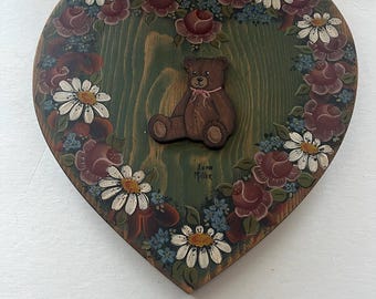 Placa de madera con forma de corazón pintada a mano, de arte popular vintage, que presenta un osito de peluche y un motivo floral.