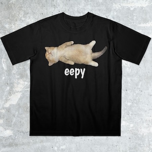 May include: Black t-shirt featuring a light brown cat lying on its back with the word "eepy" in white. The cat has its paws up and tail curled. The shirt is made of a soft material.