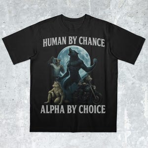 Puede incluir: Camiseta negra con un diseño de un hombre lobo aullando a la luna llena, rodeado de otras figuras de lobos. El texto "HUMAN BY CHANCE" y "ALPHA BY CHOICE" está impreso en blanco.