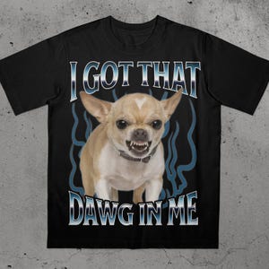 Könnte beinhalten: Schwarzes T-Shirt mit einem knurrenden Chihuahua und dem Text "I GOT THAT DAWG IN ME" in Blau und Weiß. Der Hund ist hellbraun und weiß mit einem silbernen Halsband. Blaue flammenartige Designs befinden sich hinter dem Hund.
