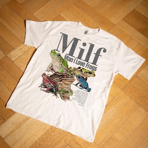 May include: A white t-shirt with a graphic print of frogs and the text "Milf Man I Love Frogs".