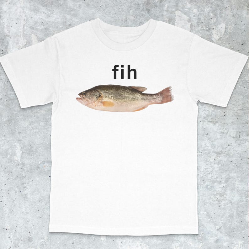 May include: White t-shirt with the word "fih" above a detailed illustration of a fish. The fish is rendered in shades of brown, grey, and pink, with visible scales and fins. The t-shirt has a crew neck design.