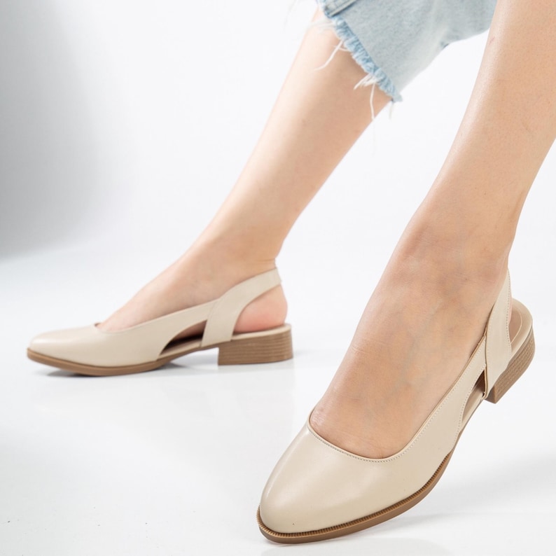 May include: A pair of beige leather heeled slingback shoes with a pointed toe. The shoes have a cut-out detail on the side and a low block heel.