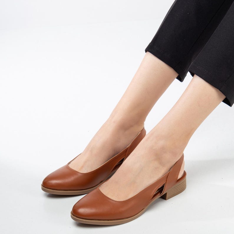 May include: A pair of brown leather slingback shoes with a low heel. The shoes have a cut-out design on the side.