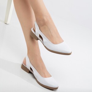 May include: White leather slingback shoes with a pointed toe and a low heel. The shoes have a cut-out design on the side.