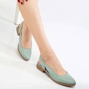 Puede incluir: Un par de zapatos planos de piel verde claro con tira trasera y punta puntiaguda y tacón bajo.