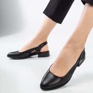 May include: Black leather slip-on shoes with a cut-out detail on the back of the heel. The shoes have a low block heel.