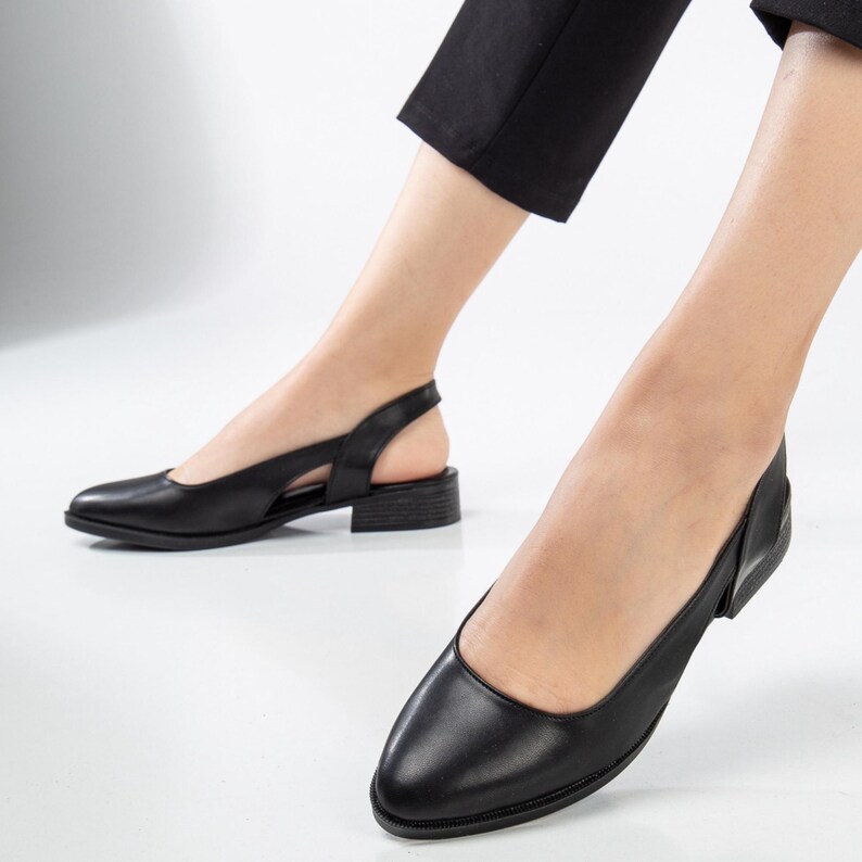 May include: Black leather slip-on shoes with a cut-out detail on the back of the heel. The shoes have a low block heel.