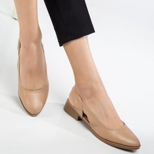 May include: A pair of beige leather slip-on shoes with a pointed toe and a small heel. The shoes have a cut-out design on the side.
