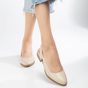 May include: A pair of beige leather slip-on shoes with a slingback strap. The shoes have a pointed toe and a low heel.