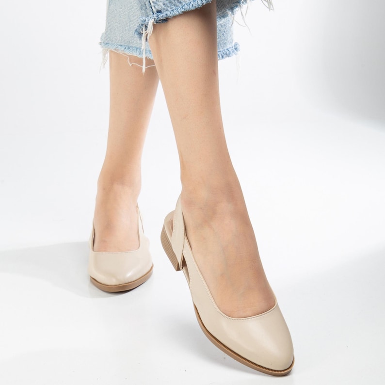 May include: A pair of beige leather slip-on shoes with a slingback strap. The shoes have a pointed toe and a low heel.