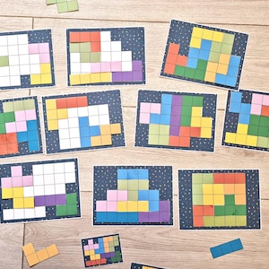 May include: A collection of colorful puzzle cards and loose puzzle pieces arranged on a wooden surface. The cards feature various pixelated designs in shades of green, yellow, blue, purple, and orange. The loose pieces are in similar colors.
