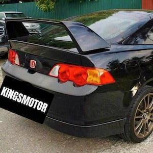 Puede incluir: Un Honda Integra Type R negro con un gran alerón trasero, luces traseras rojas y una pegatina "KINGSMOTOR" en el parachoques trasero.