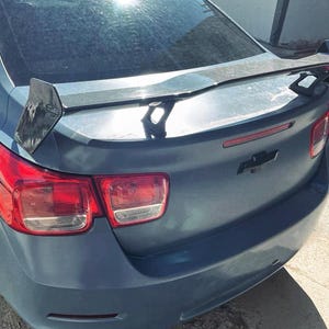 May include: A blue car with a black rear spoiler and red taillights. The car has a black rear bumper and a black license plate.