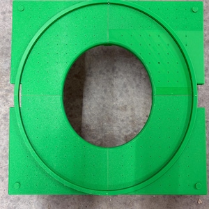 May include: Bright green, modular, circular object. The object is composed of four square sections with a circular track in the centre. The track has evenly spaced holes. The corners of the squares have small, round pegs.