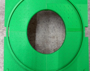 May include: Bright green, modular, circular object. The object is composed of four square sections with a circular track in the center. The track has evenly spaced holes. The corners of the squares have small, round pegs.