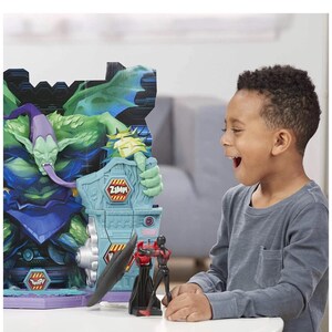 May include: A child is excited while looking at a toy playset featuring a green monster and two action figures. The playset has a blue and gray structure with the text "Zzmp!" and "Twip!" on it. One action figure is black and red.