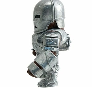 May include: A silver-colored Iron Man action figure, standing upright. The figure is wearing a detailed metallic suit with a helmet, shoulder pads, and gauntlets. The figure is a collectible item.