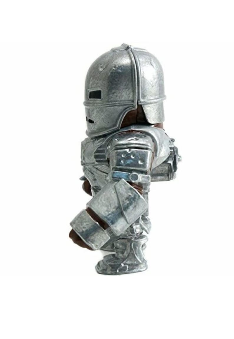 May include: A silver-colored Iron Man action figure, standing upright. The figure is wearing a detailed metallic suit with a helmet, shoulder pads, and gauntlets. The figure is a collectible item.