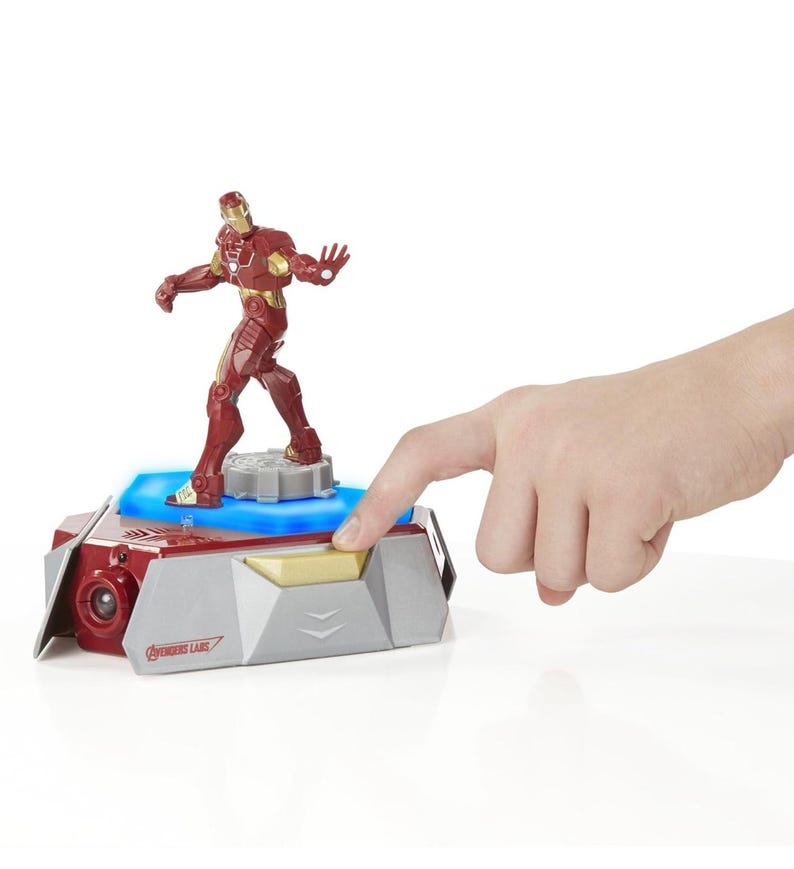 Puede incluir: Una figura de acci&oacute;n de Iron Man roja y dorada se encuentra sobre una base gris y roja con una luz azul. La base tiene un bot&oacute;n dorado y el texto "Avengers Labs".