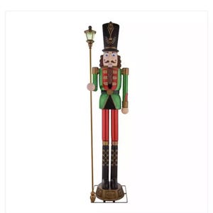 May include: A large, wooden nutcracker figurine with a green and red uniform, a black hat with gold accents, and a gold staff with a light on top. The nutcracker is standing on a gold base.