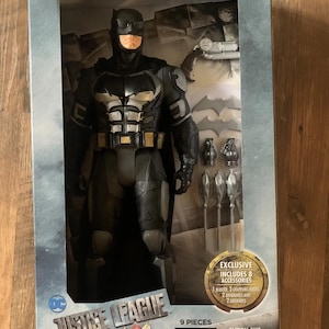 May include: A boxed Batman action figure from the Justice League series. The figure is in a black tactical suit and includes accessories. The packaging states the figure is 48 cm tall and includes 8 accessories. The box also has the text "BIG-FIGS".