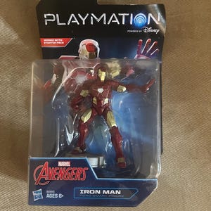 Puede incluir: Figura de acci&oacute;n de Iron Man empaquetada de la serie Marvel Avengers. La figura es roja y dorada, con el texto "IRON MAN HERO SMART FIGURE" en el embalaje. El embalaje tambi&eacute;n presenta los logotipos de Playmation y Disney.