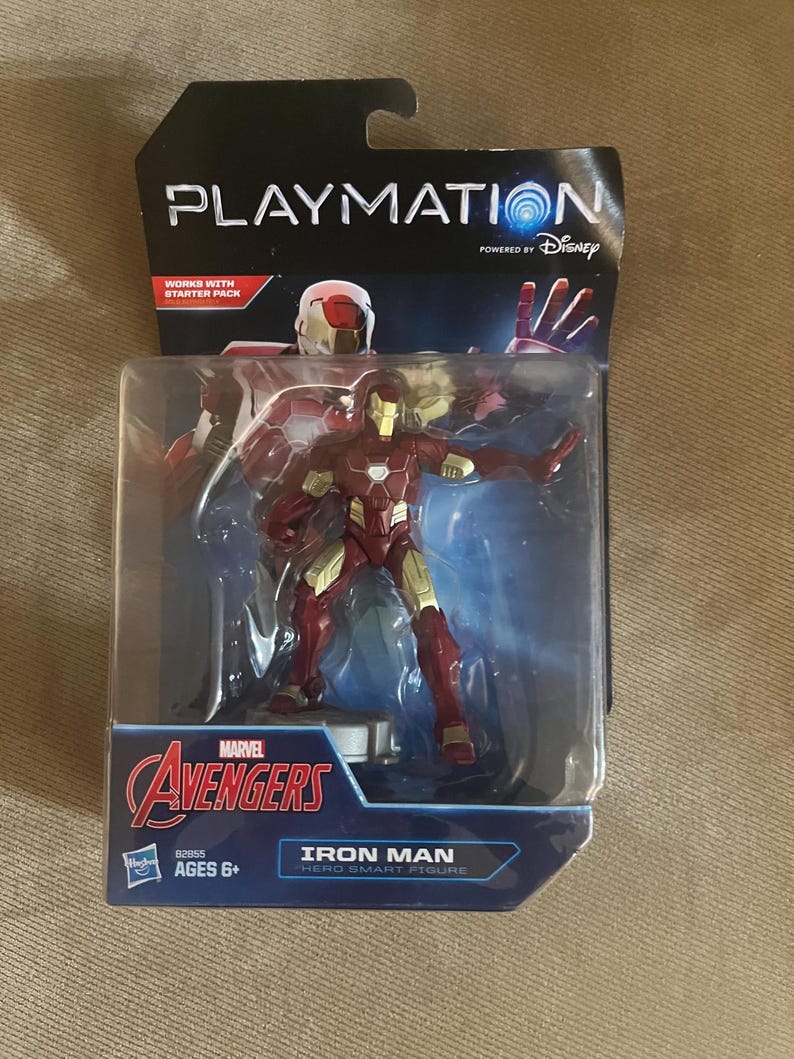 Puede incluir: Figura de acci&oacute;n de Iron Man empaquetada de la serie Marvel Avengers. La figura es roja y dorada, con el texto "IRON MAN HERO SMART FIGURE" en el embalaje. El embalaje tambi&eacute;n presenta los logotipos de Playmation y Disney.